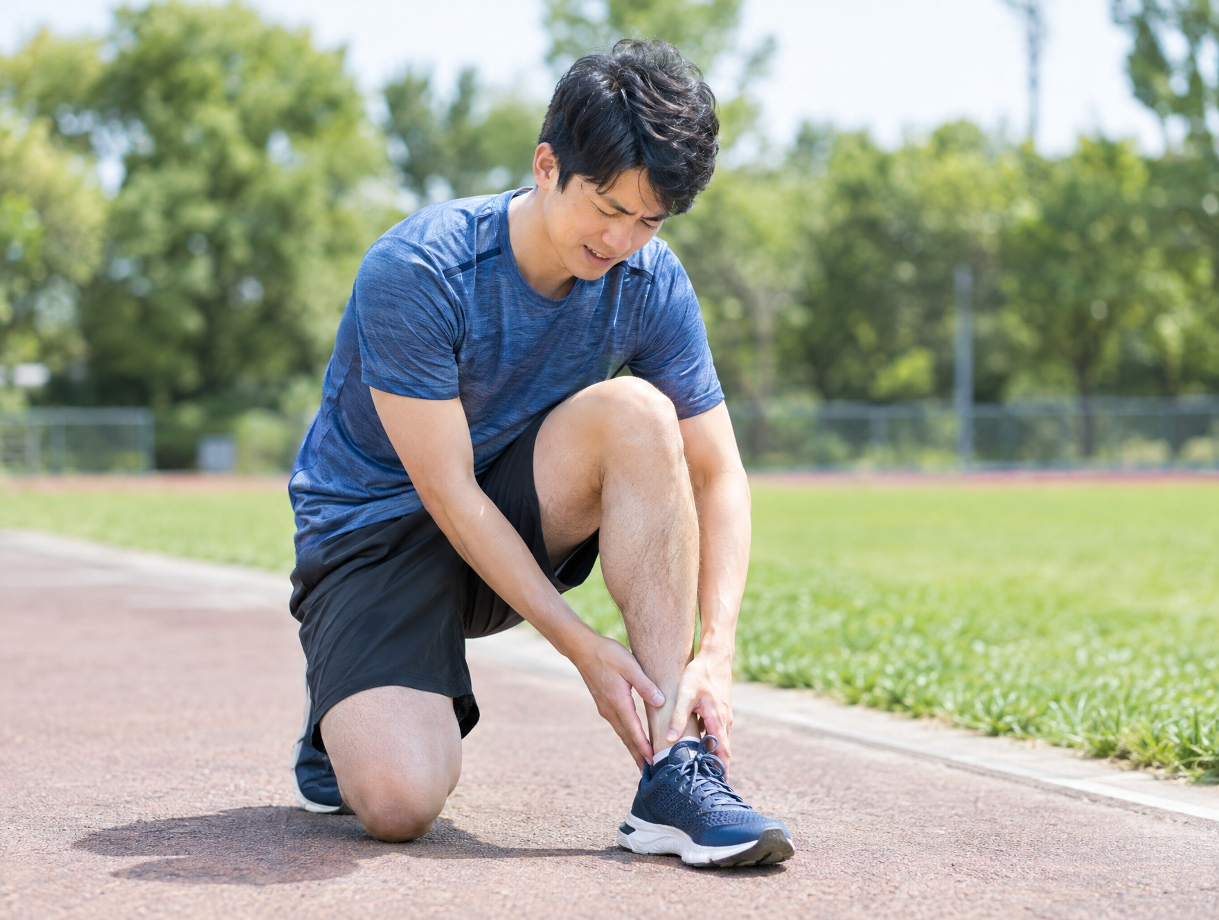スポーツ中に足首をひねって痛みをこらえている30代男性